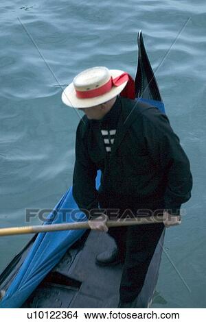 Picture - Gondolier with red ribbon straw hat on stern of gondola. Fotosearch