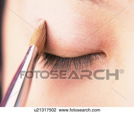 Stock Image - A Woman Applying Beige-Colored Eye Shadow, Front View, Differential Focus. Fotosearch