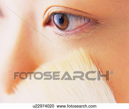 Stock Image - A Woman Applying Face Powder with a Brush, Differential Focus. Fotosearch