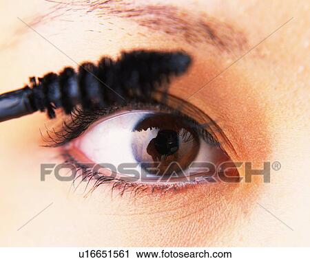 Stock Image - A Woman Applying Mascara, Front View, Looking at Camera, Differential Focus. Fotosearch
