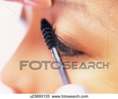 Stock Image - A Woman Applying Mascara, Side View, Differential Focus. Fotosearch