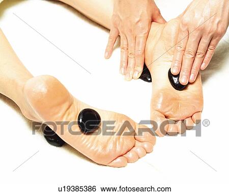 Stock Photograph - Aesthetician Who Pushes Woman's Foot With Stones, High Angle View. Fotosearch