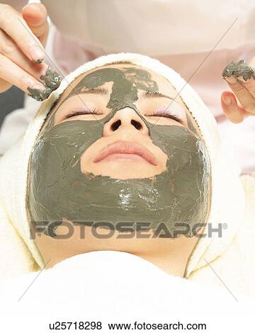 Stock Photo - Aesthetician Who Rubs Mud Pack on Woman's Face, High Angle View. Fotosearch