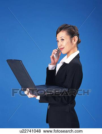 Stock Photo - Businesswoman holding mobile phone on one hand and laptop computer on the other, Studio, Portrait. Fotosearch