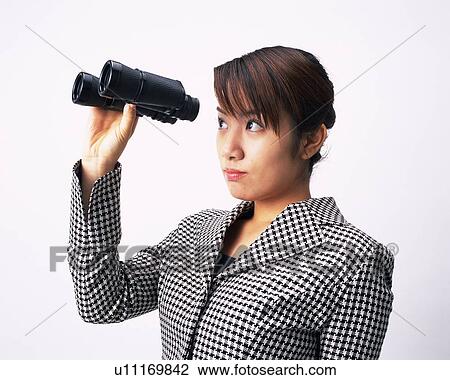 Stock Image - Businesswoman looking into a pair of binoculars, Studio, Portrait. Fotosearch