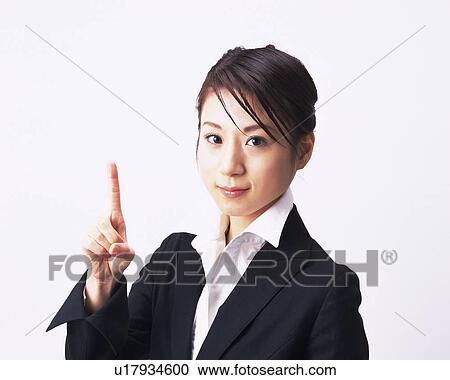 Stock Image - Businesswoman pointing up with index finger, Studio, Portrait. Fotosearch