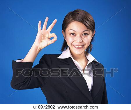 Stock Image - Businesswoman smiling with finger sign, Studio, Portrait. Fotosearch