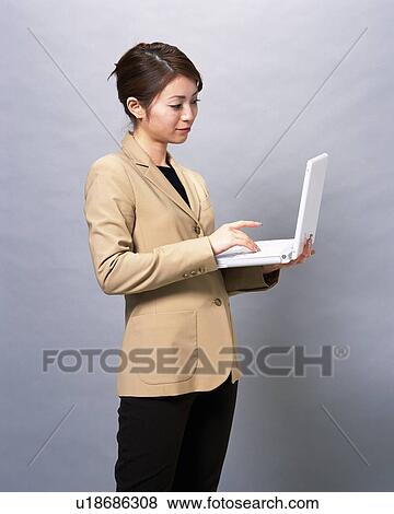 Stock Photo - Businesswoman standing and working on laptop computer, Studio, Portrait. Fotosearch