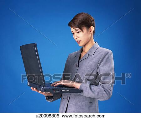 Stock Photograph - Businesswoman standing and working on laptop computer, Waist Up, Studio, Portrait. Fotosearch
