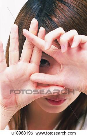 Stock Photography - Closed Up Image of a Young Adult Woman Forming Something With her Hands, Peeping Through Them with one Eye, High Angle View. Fotosearch