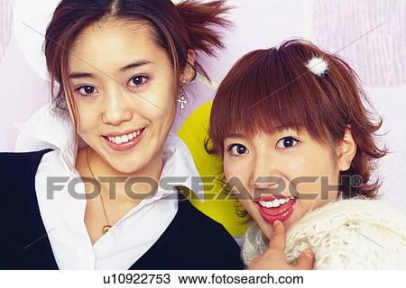 Stock Image - Closed Up Image of Two Young Adult Women Standing In Front Of Polka Dot Wall, Front View, Looking at Camera. Fotosearch