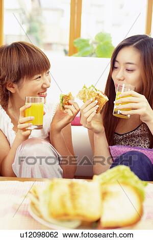 Stock Image - Two Young Adult Women Eating Sandwiches, Differential Focus, High Angle View. Fotosearch
