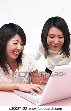 Stock Image - Two Young Adult Women Operating a Laptop, Smiling, Side View. Fotosearch