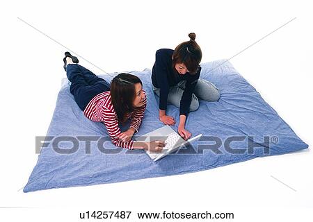 Stock Photo - Two Young Adult Women Operating a Laptop on a Blue Blanket, Smiling, High Angle View. Fotosearch