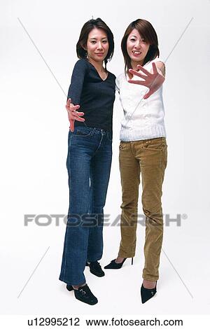 Stock Image - Two Young Adult Women Reaching Out Their Hands and Posing, Looking at Camera, Front View, Low Angle View. Fotosearch