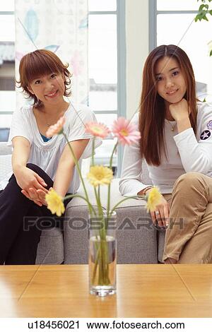 Two Young Adult Women Sitting on a Couch and Flowers on the Table, Front View, Looking at Camera, Smiling View Large Photo Image Stock Image - Two Young Adult Women Sitting on a Couch and Flowers on the Table, Front View, Looking at Camera, Smiling. Fotosearch