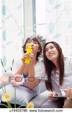 Two Young Adult Women Sitting on a Couch, One Blowing Soap Bubbles, Front View, Differential Focus View Large Photo Image Stock Photograph - Two Young Adult Women Sitting on a Couch, One Blowing Soap Bubbles, Front View, Differential Focus. Fotosearch