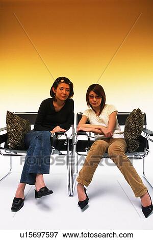 Two Young Adult Women Sitting on Chairs With a Fading Brown Backround, Front View, Looking at Camera View Large Photo Image Stock Photo - Two Young Adult Women Sitting on Chairs With a Fading Brown Backround, Front View, Looking at Camera. Fotosearch