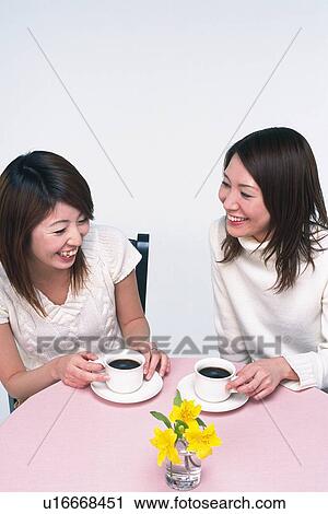 Stock Image - Two Young Adult Women Talking and Laughing While Having Coffee, High Angle View. Fotosearch