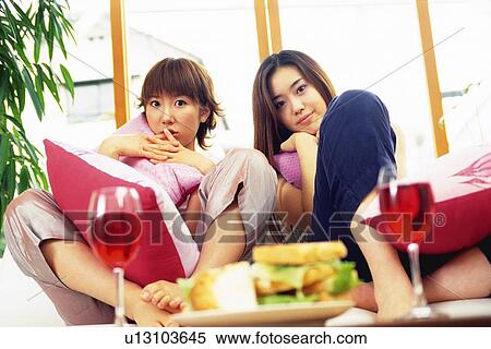 Stock Photography - Two Young Adult Women with Sandwiches and Wine, Sitting on a Couch, Looking at Camera, Low Angle View. Fotosearch
