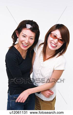 Stock Image - Two Young Adult Women With Sunglasses Holding Each Other, Smiling, Looking at Camera, High Angle View, Side View. Fotosearch