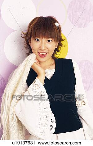 Stock Image - Young Adult Woman Holding a Stole, Standing In Front Of Polka Dot Wall, Looking at Camera, Smiling, Front View. Fotosearch