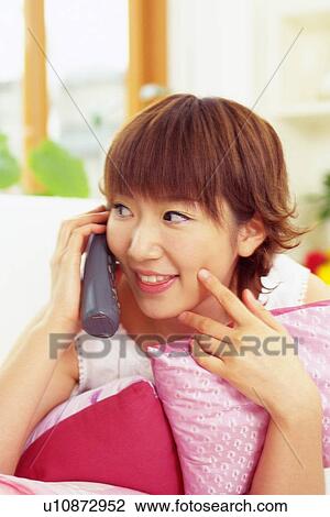 Stock Image - Young Adult Woman Talking on the Phone, Smiling and Looking Sideways, Front View, Differential Focus. Fotosearch