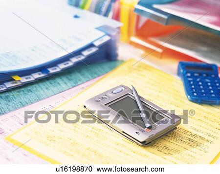 Stock Image - Personal digital assistant on files piled up on desk. Fotosearch