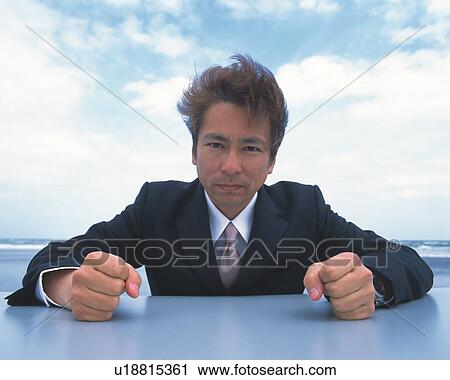 Stock Image - Closed Up Image of a Businessman Having his Fists on a Table at the Beach, Looking at Camera, Front View. Fotosearch