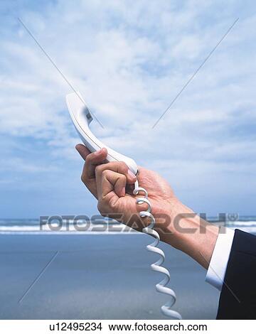 Picture - Closed Up Image of a Male Hand Holding a White Telephone Receiver Under a Cloudy Sky, Low Angle View. Fotosearch