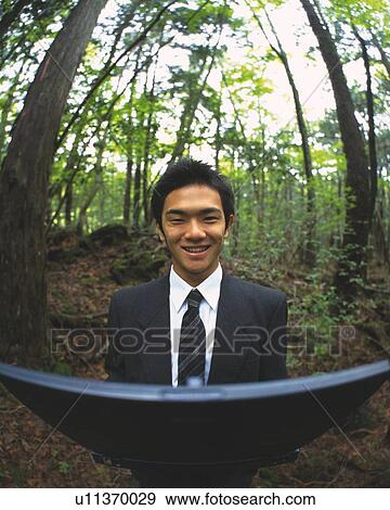 Stock Photo - Image of a Businessman Holding a Laptop in the Middle of a Forest, Smiling, Looking at Camera, High Angle View, Fish Eye. Fotosearch