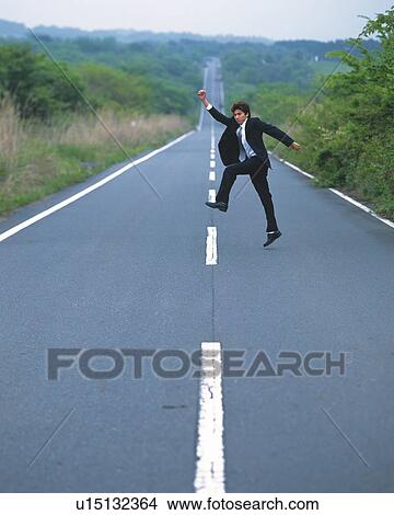 Picture - Image of a Businessman Jumping in the Air on the Middle of a Road, High Angle View, Side View. Fotosearch