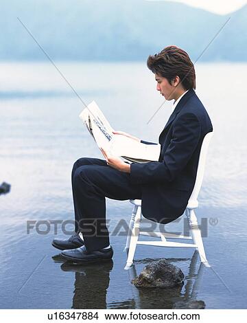 Picture - Image of a Businessman Sitting on a Chair Reading a Newspaper at the Beach, Side View. Fotosearch