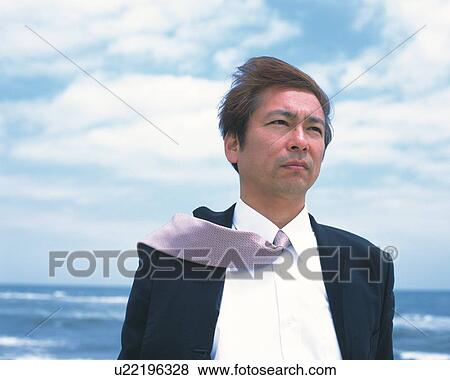 Stock Photo - Image of a Businessman Standing at the Beach Under a Blue Sky, the Wind Blowing, Low Angle View. Fotosearch