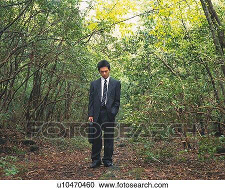 Stock Image - Image of a Businessman Standing in the Middle of a Forest With a Suitcase in his Hand, Front View. Fotosearch