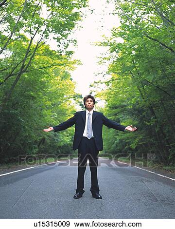 Stock Photo - Image of a Businessman Standing in the Street with his Arms wide Open, Surrounded By Trees, Front View, Looking at Camera. Fotosearch