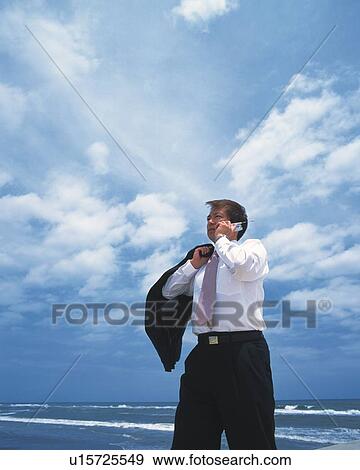 Stock Photo - Image of a Businessman Talking on his Cell Phone at the Beach Under a Blue Sky, Low Angle View. Fotosearch