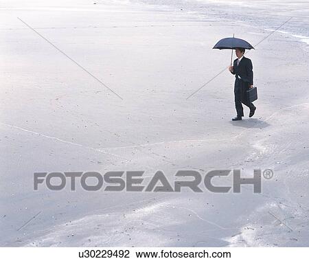 Stock Image - Image of a Businessman Walking Along the Beach With an Umbrella, High Angle View, Side View, Copy Space. Fotosearch