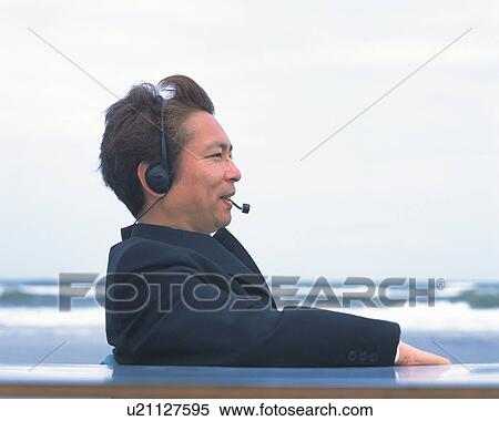 Stock Photography - Image of a Businessman Wearing a Headset, Smiling at the Beach, Side View, Differential Focus. Fotosearch