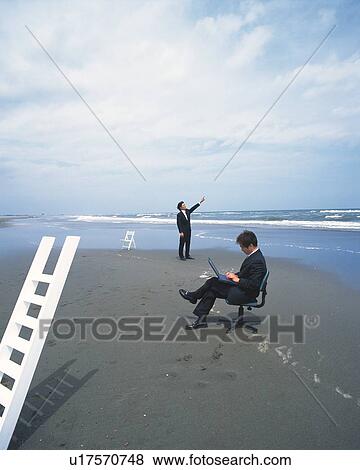 Stock Photo - Image of Two Businessmen at the Beach, the One Using a Laptop, the Other One Pointing at the Sky, Far View, Side View. Fotosearch