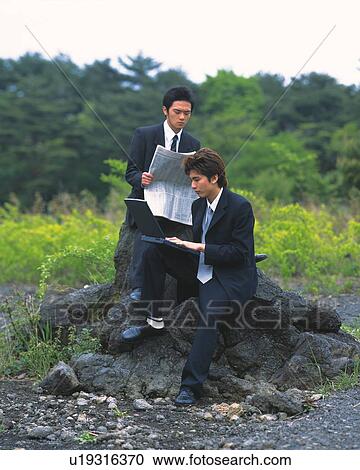 Stock Image - Image of Two Businessmen Sitting on a Rock, the One working at his Laptop, the Other One Reading a Newspaper, Front View, Side View. Fotosearch