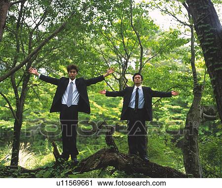 Stock Image - Image of Two Businessmen Standing in a Forest With Their Arms Wide Open, Low Angle View, Looking at Camera. Fotosearch