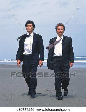 Stock Photograph - Image of Two Businessmen Walking at the Beach, the Wind Blowing Through Their Hair, Front View. Fotosearch