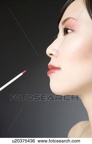 Stock Photograph - Young Woman Applying Lipstick with Lip Brush. Fotosearch