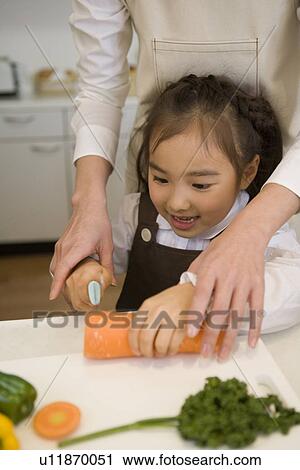 Stock Image - Girl trying to cutting a carrot. Fotosearch