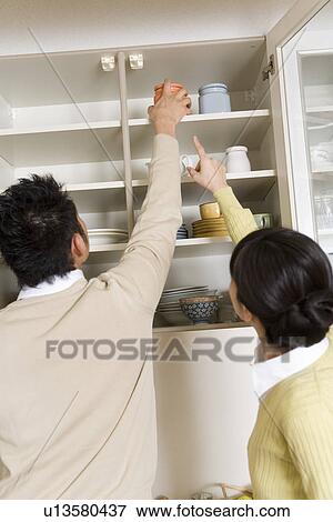 Husband helping to get table ware from the kitchen cabinet View Large Photo Image Stock Photo - Husband helping to get table ware from the kitchen cabinet. Fotosearch