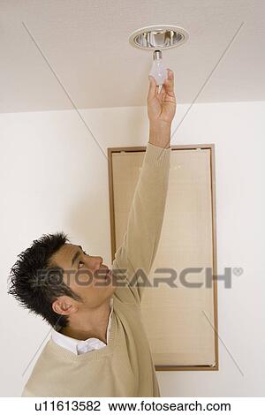 Mid Adult Man reaching to change the light bulb View Large Photo Image Stock Image - Mid Adult Man reaching to change the light bulb. Fotosearch