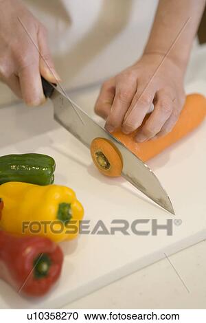 Stock Image - Mid Adult Woman cutting a carrot. Fotosearch