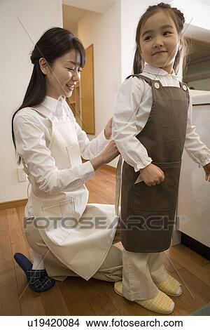 Picture - Mid Adult Woman helping to tie daughter's apron. Fotosearch