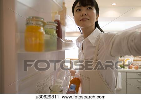 Stock Image - Mid Adult Woman looking at inside of the fridge. Fotosearch